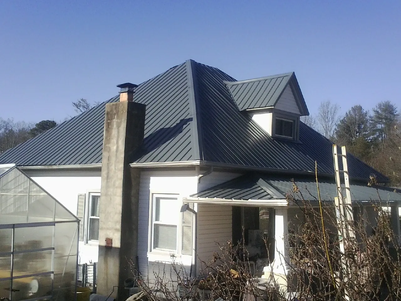 Dark blue standing seam metal roof on a white farmhouse with dormer — Slate & Tile Roof Repair by Roofing Brothers in West Sayville