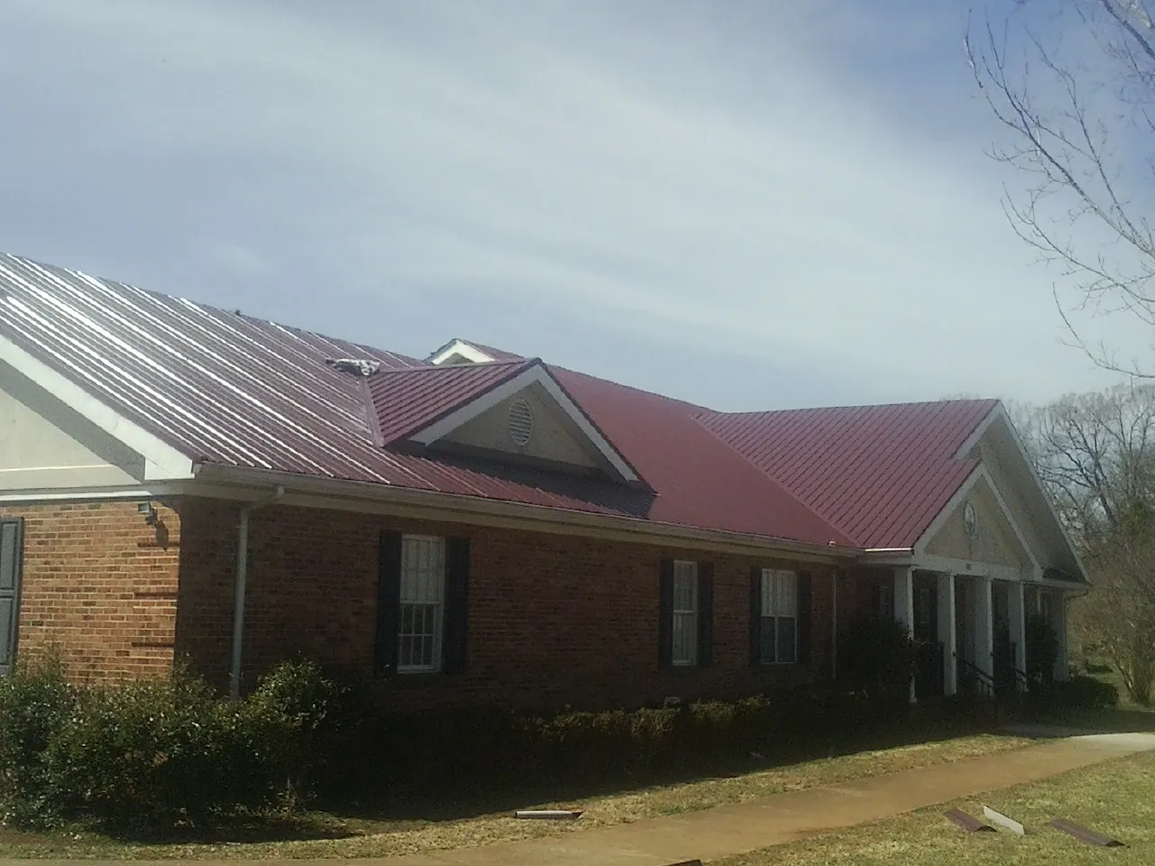 Red metal roof with gabled entries on a long brick building, from a Hail Damage Roof Repair job in West Sayville