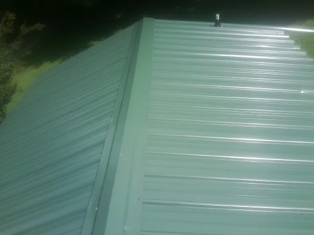 New green metal panels meeting at the ridge of a roof — Flat Roof Repair work by our crew in West Sayville