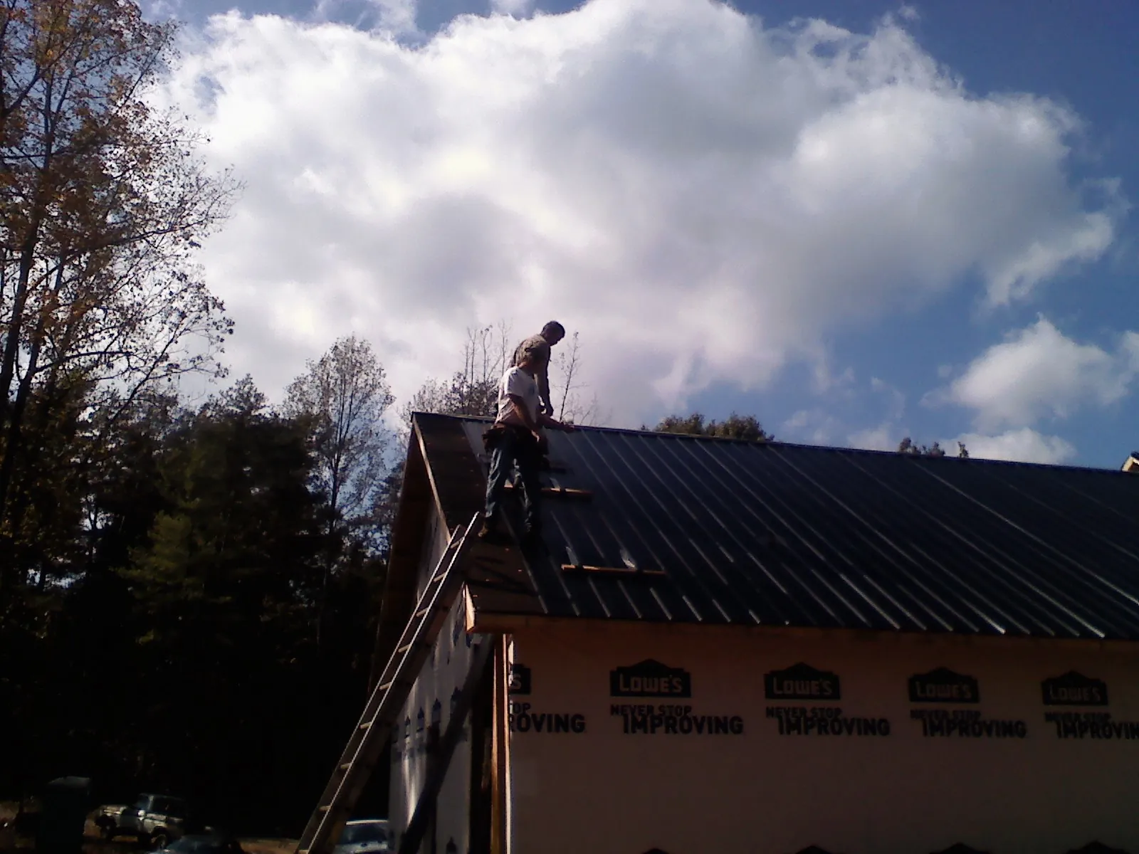 Roofer fastening dark metal panels high against a cloudy sky, from a Roof Inspection job in West Sayville