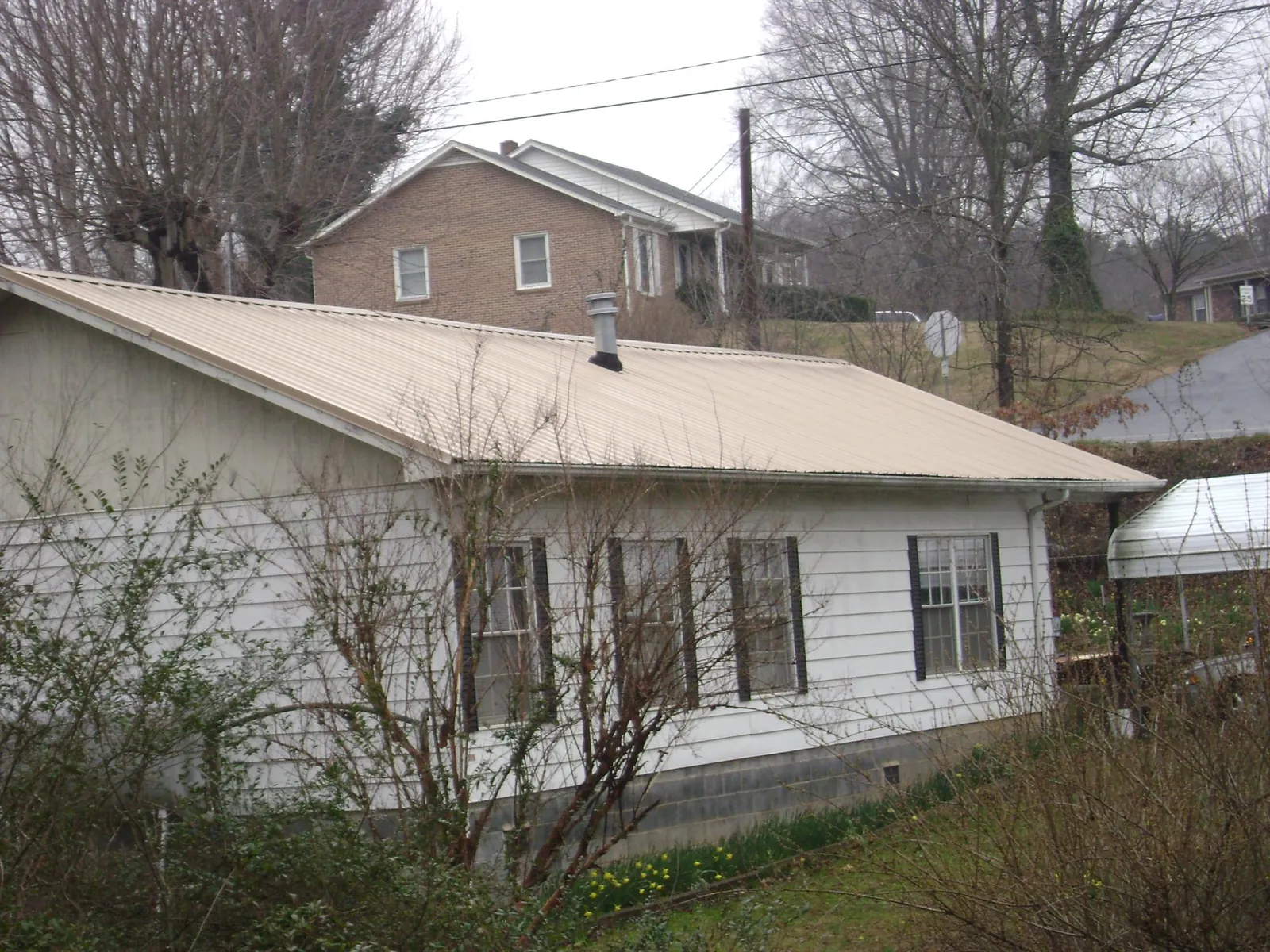 Tan metal roof on a white sided house set into a hillside — Commercial Roofing by Roofing Brothers in West Sayville
