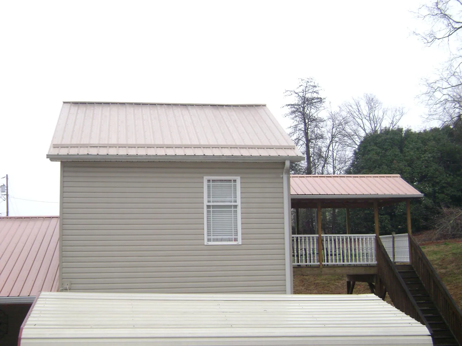 Tan metal roofs on a two story addition and attached porch, from a Roof Replacement job in West Sayville